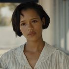 Eine Frau hält eine Glühbirne und steht in einem Flur, ihr Ausdruck ist ruhig und nachdenklich.