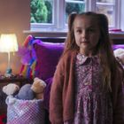 Der Text an der Wand sagt "happy". Ein kleines Mädchen steht in einem gemütlichen Kinderzimmer mit Kuscheltieren.