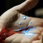 Blut und blaue Flüssigkeit vermischen sich in einer geöffneten Handfläche.