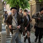 Mehrere Menschen in historischer Kleidung, teils bewaffnet, bewegen sich entschlossen durch einen alten Friedhof.