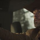 Ein Mann mit Bart und Cowboyhut fährt konzentriert ein Auto.