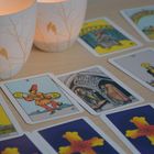 "Page der Münzen." Tarotkarten mit farbenfrohen Illustrationen liegen auf einem Tisch neben zwei Lichtkerzen.