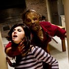 Eine Person hält eine andere bedrohend am Hals. Beide sind in einem Raum mit Backsteinen im Hintergrund.