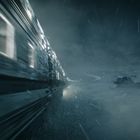 Ein Zug bewegt sich in hoher Geschwindigkeit durch eine winterliche Schneelandschaft, in der Ferne sind Berge zu sehen.