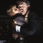 Ich kann den Text nicht erkennen. Ein Mann umarmt erschrocken eine Frau und beide blicken in die Kamera.