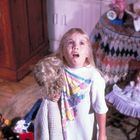 Mädchen mit weißem T-Shirt und buntem Obstmotiv, schaut erschrocken. In der Hand hält sie eine blonde Puppe.