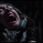 Eine Frau schreit mit weit geöffnetem Mund. Krallenartige Hände halten ihren Hals fest.