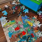 Auf einem Puzzle steht in geschwungenen Buchstaben „Ein Buch“. Dargestellt sind grüne Comic-Drachen beim Spielen.