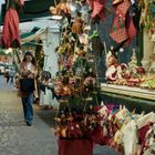 Schilder mit "Welcome" und "Strega Nera". Eine Frau spaziert an einem farbenfrohen Marktstand voller Dekorationen vorbei.