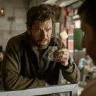 Ein Mann mit ernstem Blick zeigt ein kleines Foto. Im Hintergrund sind mehrere Personen in einem ruhigen Raum.