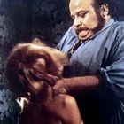 Es gibt keinen Text. Ein großer Mann hält eine Person fest, sein Gesicht wirkt angespannt. Hintergrund ist gemustert.