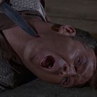 Es gibt keinen Text. Ein Mann liegt mit weit geöffnetem Mund am Boden, ein Messer wird an seinen Hals gehalten.