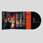 "STRANGERS (AGAIN)" steht in weißer Schrift über abgedruckten Texten. Ein Mann steht in einem schmalen, hell erleuchteten Gang.