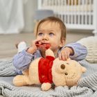 Ein Baby liegt auf einem grauen Strickdeckchen und hält ein Stofftier in rotem Pullover. Es schaut nach oben.