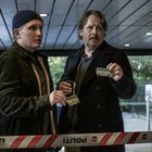 Zwei Männer zeigen Presseausweise. Ein Polizeiband mit "POLITI STOP" trennt sie vorne. Sie schauen ernst.