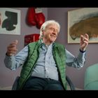 Rote Boxhandschuhe, Gemälde, lachender älterer Mann mit grünem Gilet, hellblaues Sofa, lila Wand.