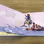 Text: "Paddington loves helping others! When he went to the seaside, he rescued this dolphin and made a new friend!” 

Illustration: Paddington auf einem Delfin, Kinder auf einem Boot, welliges Wasser.