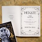Auf einer geöffneten Buchseite steht: "HEKATE, THE WITCH, GODDESSES OF THE UNDERWORLD, NIKITA GILL." Daneben liegt ein Buchcover.