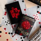 Buch "Bad Blood" von Jennifer Lynn Barnes, umgeben von Spielkarten, Puzzleteilen und einem Notizbuch mit rotem Motiv.