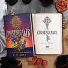 "CURSEBREAKER" von R. M. Gray, ein Buch mit einem Bild von einem verzierten Schlüssel über blauen Blumen.