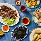 Ein Tisch mit Entenfleisch, Gurkenstreifen, Frühlingsrollen, Sesam-Toast, frittierten Teigtaschen und mehreren Soßen.