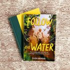 "FOLLOW THE WATER" von Ellen Cochrane. Eine Frau steht im Wasser, umgeben von grüner Vegetation.
