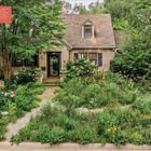 Text: "Post-lawn, the gravel garden is the perfect solution..."  
Eine gepflegte, grüne Landschaft umgibt ein gemütliches Haus.