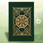 Ein dunkelgrünes Buch mit goldener, verzierter Mandala-Dekoration. Im Hintergrund sind helle Grüntöne und eine weiße Blume.