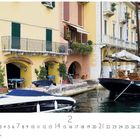 Text: „Malcesine“. Unten sind die Zahlen 1 bis 28 aufgelistet, ein Kalenderblatt. Szene: Boote vor bunten Häusern am Wasser.