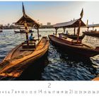 „Dubai, Bay Creek“. Zwei Holzboote auf ruhigem Wasser mit Gebäuden im Hintergrund. Datum 2 markiert, Serie CASAERS EDITION.