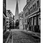 Kalenderblatt mit Text "The Shard", Datum "2" und Kalendertage darunter. Kopfsteinpflasterstraße führt zu moderner Architektur.
