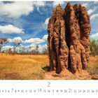 "Kakadu National Park." Hoher Termitenhügel, umgeben von trockener Vegetation, unter blauem Himmel mit Wolken.