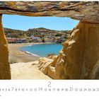 Kreta, Matala. Sandstrand und blaues Meer, umrahmt von Felsen. Kleine Stadt im Hintergrund.