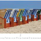Strandkörbe auf Amrum. Mehrere bunte Strandkörbe stehen in einer Reihe auf hellem Sand am Strand unter einem blauen Himmel.