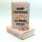 "Audrey Niffenegger, Die Unruhe der Zeit. Roman." Das Cover zeigt dekorative orange Blüten auf einem hellen Hintergrund.