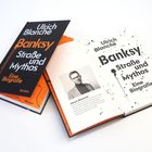 „Ulrich Blanché: Banksy. Straße und Mythos. Eine Biografie.“ Zwei Bücher, eines aufgeschlagen, mit Autorbild.
