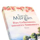 Buchtitel: "Das Geheimnis unseres Sommers" von Sarah Morgan, Roman. Blütenmuster am oberen Rand.