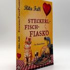 Rita Falks "Steckerlfischfiasko". Ein Provinzkrimi. Vordergrund: Katze, Fisch, Getränke; Hintergrund: rote Tischdecke.