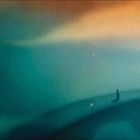 Eine neblige Landschaft mit einer einsamen Figur auf einer Brücke, beleuchtet von kleinen Lichtern, in Blau- und Orangetönen.