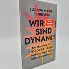 Text auf dem Buchcover: "Juliane Marie Schreiber, WIR SIND DYNAMIT, Ein Manifest für INTROVERTIERTE in einer Welt der Selbstdarstellung". Auf dem Cover sind stilisierte gelbe und orangefarbene Explosionen. Es handelt sich um einen Stapel Bücher.