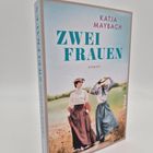 Aufrecht stehender Roman "Zwei Frauen" von Katja Maybach. Illustration: Zwei Frauen in historischer Kleidung auf einem Feld.