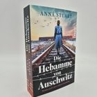 „Die Hebamme von Auschwitz“ von Anna Stuart, Buchstapel, Frau auf Gleis, Vögel, Himmel, Gebäude.