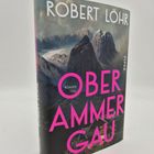 Buchtitel: "OBERAMMERGAU" von Robert Löhr. Berglandschaft im Hintergrund, dunkle Töne, pinke Schrift.