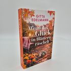 Text: "Wenn das Glück in Blättern raschelt" - Roman von Gitta Edelmann. Ein Igel in einem herbstlichen Garten mit Blumen.