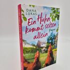 „Ein Huhn kommt selten allein“ von Dana Lukas. Zwei Hühner und ein Küken vor einem Haus mit grünem Garten.