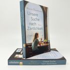 Ein Buchcover zeigt "Unsere Suche nach Zärtlichkeit" von Martin Ehrenhauser. Darauf eine Person allein am Tisch am Fenster.