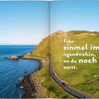 Text: "Fahr einmal im Jahr irgendwohin, wo du noch nie warst." Küstenstraße und Meer unter blauem Himmel.