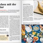 **Kochen mit der Natur** steht groß oben. Text über die nordische Küche füllt die linke Seite. Rechts oben ein Hering auf einem Teller. Unten ein reich gedeckter Tisch mit Essen.