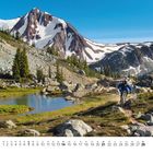 Monat "2", Kalenderdaten darunter. Berglandschaft mit Radfahrer, See, Bäumen und schneebedeckten Gipfeln.