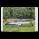 Ein gepflegter Garten mit Teich, Terrasse, Blumen und Backsteinmauer. Im Hintergrund sind dichte Bäume.